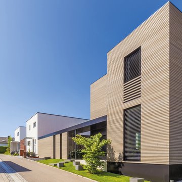 A photograph of sleek, modern timber-clad houses in a newly built housing development on a sunny day.